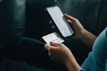 A credit card in the hands of a young businesswoman pays for a business on a mobile phone and on a desk with a laptop.の写真素材