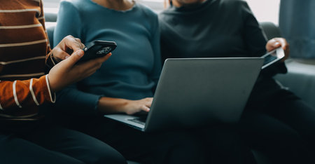 Three beautiful Asian girls using smartphone and laptop, chatting on sofa together at cafe with copy space, modern lifestyle with gadget technology or working woman on casual business conceptの写真素材