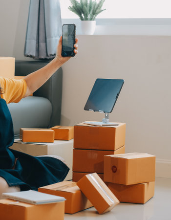 Startup SME small business entrepreneur of freelance Asian woman wearing apron using laptop and box to receive and review orders online to prepare to pack sell to customers, online sme business ideas.の写真素材