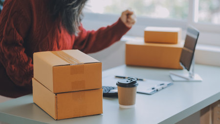 Startup SME small business entrepreneur of freelance Asian woman using a laptop with box Cheerful success Asian woman her hand lifts up online marketing packaging box and delivery SME idea conceptの写真素材