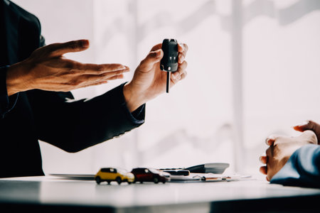 A car rental company employee is handing out the car keys to the renter after discussing the rental...