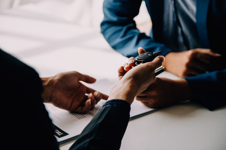 A car rental company employee is handing out the car keys to the renter after discussing the rental details and conditions together with the renter signing a car rental agreement. Concept car rental.の写真素材