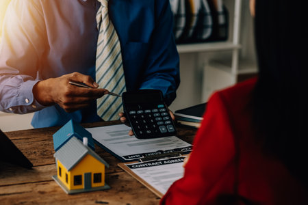 Real estate broker agent presenting and consult to customer to decision making sign insurance form agreement, buy and sell home model, concerning mortgage loan offer for and house insuranceの写真素材