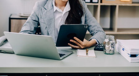 Asian Business woman using calculator and laptop for doing math finance on an office desk, tax, report, accounting, statistics, and analytical research conceptの写真素材