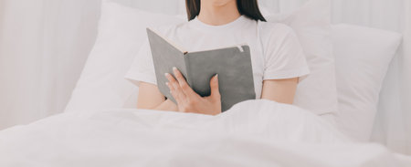 Efficient Young Millennial Girl Sitting on a Bed in the Morning, Uses Laptop Computer and Eats Croissants and Drinks Coffee for Breakfastの写真素材
