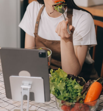 Delicious fruit and vegetables on a table and woman cooking. Housewife is cutting green cucumbers on a wooden board for making fresh salad in the kitchen.の写真素材