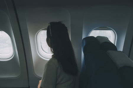 Silhouette of woman looks out the window of an flying airplane. Passenger on the plane resting beside the window.の写真素材