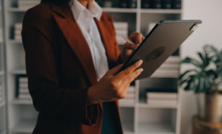 Portrait of Young Asian woman hand freelancer is working her job on computer tablet in modern office. Doing accounting analysis report real estate investment data, Financial and tax systems concept.の写真素材