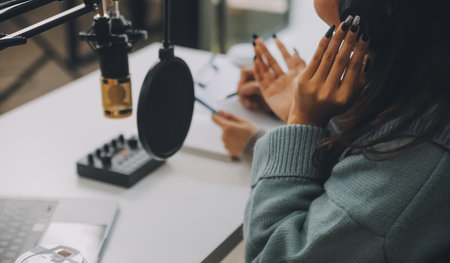 Woman recording a podcast on her laptop computer with headphones and a microscope. Female podcaster making audio podcast from her home studio.の写真素材