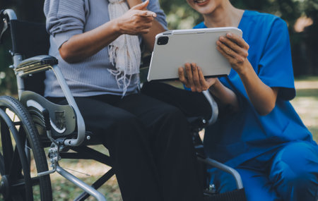 Elderly asian senior woman on wheelchair with Asian careful caregiver and encourage patient, walking in garden. with care from a caregiver and senior health insurance in sun lightの写真素材