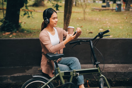 Happy young Asian woman while riding a bicycle in a city park. She smiled using the bicycle of transportation. Environmentally friendly concept.の写真素材