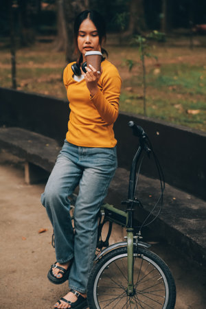 Happy young Asian woman while riding a bicycle in a city park. She smiled using the bicycle of transportation. Environmentally friendly concept.の写真素材