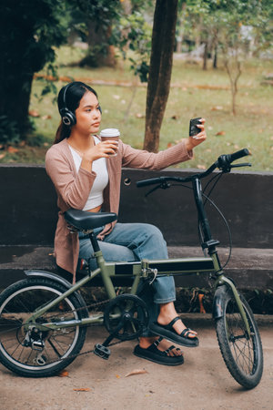 Happy young Asian woman while riding a bicycle in a city park. She smiled using the bicycle of transportation. Environmentally friendly concept.の写真素材