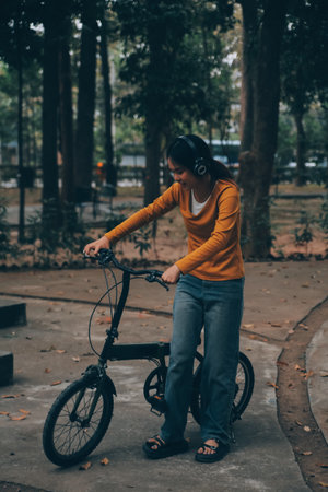 Happy young Asian woman while riding a bicycle in a city park. She smiled using the bicycle of transportation. Environmentally friendly concept.の写真素材