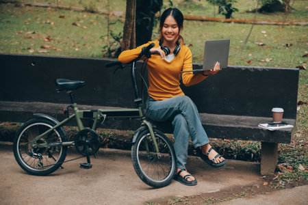 Happy young Asian woman while riding a bicycle in a city park. She smiled using the bicycle of transportation. Environmentally friendly concept.の写真素材