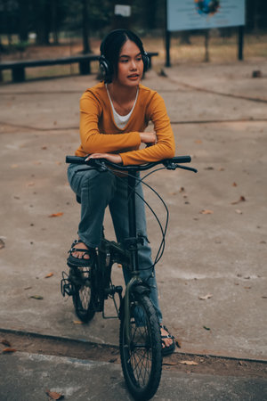 Happy young Asian woman while riding a bicycle in a city park. She smiled using the bicycle of transportation. Environmentally friendly concept.の写真素材