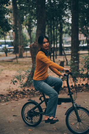 Happy young Asian woman while riding a bicycle in a city park. She smiled using the bicycle of transportation. Environmentally friendly concept.の写真素材