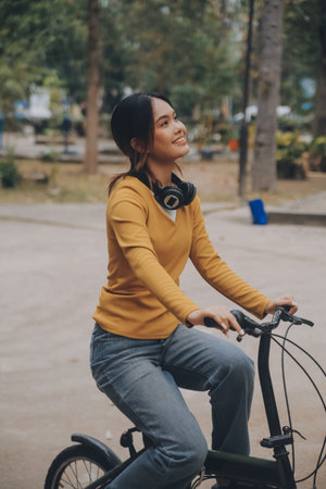 Happy young Asian woman while riding a bicycle in a city park. She smiled using the bicycle of...