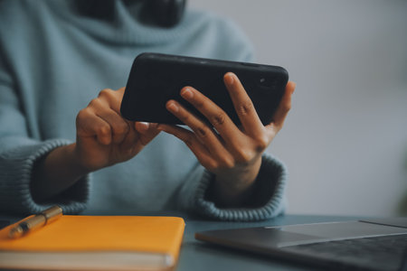 Happy pretty millennial Indian girl relaxing at home, resting in armchair, typing on smartphone, using online app, software, shopping on Internet, making video call. Mobile phone communicationの写真素材