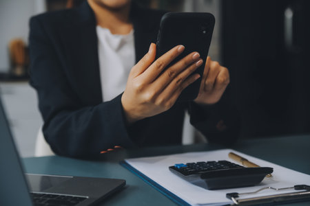 Hispanic businesswoman in formal attire in her office happy and cheerful while using smartphones and working. Young businesswoman using apps on cell phones, reading news, fast connectionの写真素材