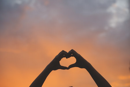 Silhouette of hands in heart symbol around the sun