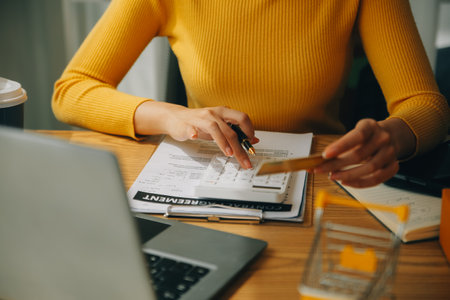 Young woman holding a smartphone, tablet showing payment success and credit card with yellow parcel box as online shopping concept in officeの写真素材