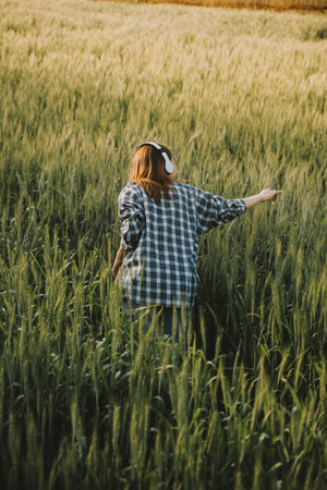 Young pretty woman in red summer dress and straw hat walking on yellow farm field with ripe golden wheat enjoying warm evening.の写真素材