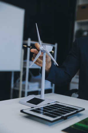 Two Young Engineers Expertise in Solar Cell Installation Meetings and Discussion in The Job. Planning to Install Solar Photovoltaic Panels on Roof Top in The Office Room with Factory Building Plan.の写真素材