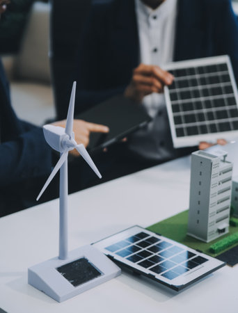 Two Young Engineers Expertise in Solar Cell Installation Meetings and Discussion in The Job. Planning to Install Solar Photovoltaic Panels on Roof Top in The Office Room with Factory Building Plan.の写真素材