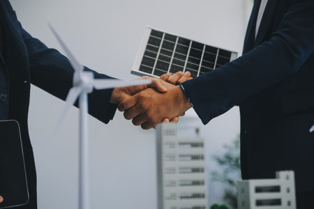 Two Young Engineers Expertise in Solar Cell Installation Meetings and Discussion in The Job. Planning to Install Solar Photovoltaic Panels on Roof Top in The Office Room with Factory Building Plan.の写真素材