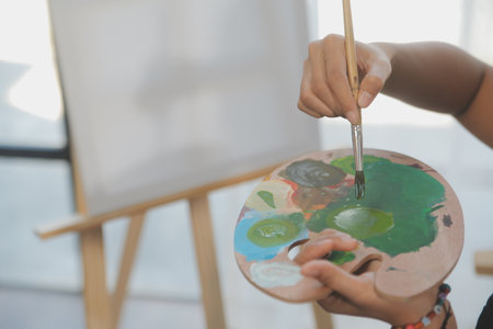 Cropped image of female artist standing in front of an easel and dipping brush into color paletteの写真素材