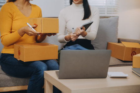 Asian SME business women use laptop computer checking customer order online shipping boxes at home....