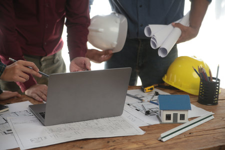 Engineers are consulting the team to design an architectural structure for clients with blueprints and building models to work at office.の写真素材