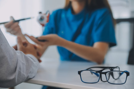 Close-up of Asian female doctor talking with elderly patient showing eyeball model and explaining eye disease in hospitalの写真素材