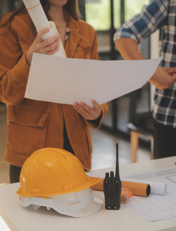 Male and Female Industrial Engineers in Hard Hats Discuss New Project while Using Laptop. They Make Showing Gestures.They Work in a Heavy Industry Manufacturing Factory.の写真素材