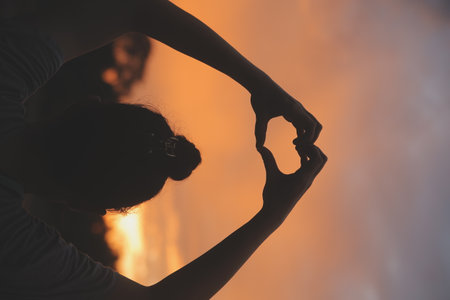 Silhouette of hands in heart symbol around the sunの写真素材