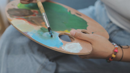 Cropped image of female artist standing in front of an easel and dipping brush into color paletteの写真素材