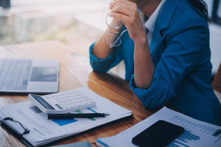Asian Business woman using calculator and laptop for doing math finance on an office desk, tax, report, accounting, statistics, and analytical research conceptの写真素材