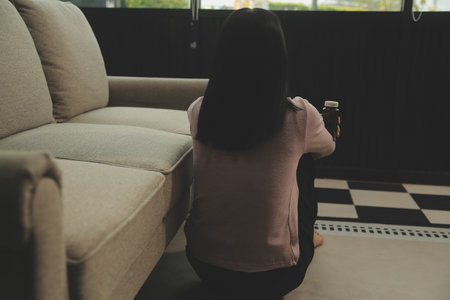 Depressed woman sitting alone on the bed with hands on head feel stress, sad and worried in the dark bedroom and low light environmentの写真素材