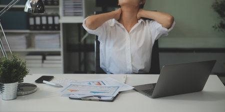 Young Asian woman feeling migraine head strain. Tired, Overworked businesswoman financier while working on laptop computer in office.の写真素材