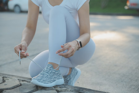 Mature fitness woman tie shoelaces on road. Cheerful runner sitting on floor on city streets with mobile and earphones wearing sport shoes. Active latin woman tying shoe lace before running.の写真素材