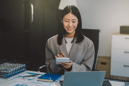 Asian woman entrepreneur using a calculator calculating financial expense at home office, press calculator button finance analyzing E-payment technology, shopaholic lifestyle, mobile applicationの写真素材