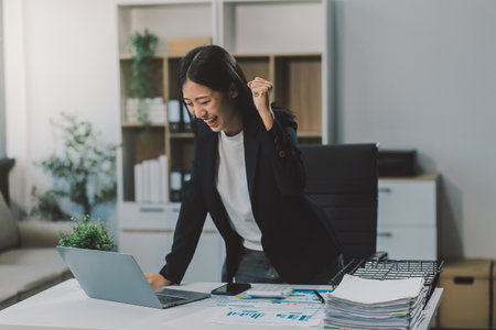 Beautiful Asian girl celebrate with laptop, success happy pose. E-commerce, university education, internet technology, or startup small business concept. Modern office or living room with copy spaceの写真素材