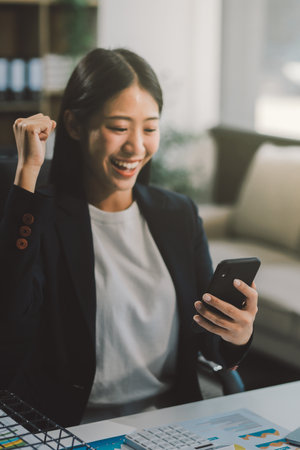Beautiful Asian girl celebrate with laptop, success happy pose. E-commerce, university education, internet technology, or startup small business concept. Modern office or living room with copy spaceの写真素材