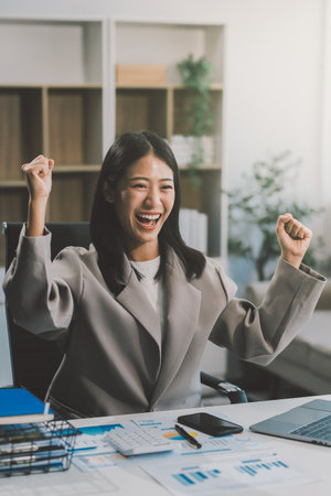 Beautiful Asian girl celebrate with laptop, success happy pose. E-commerce, university education, internet technology, or startup small business concept. Modern office or living room with copy spaceの写真素材