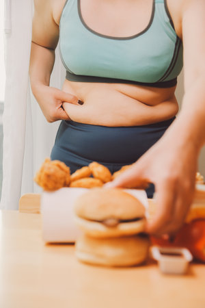To eat or not. Cheerless plump woman looking at the burger while thinking to eat it or notの写真素材