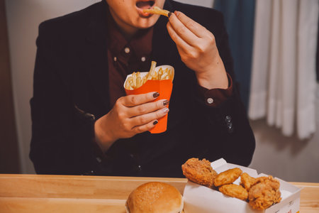 Asian woman holding french fries and eating happily in restaurantの写真素材