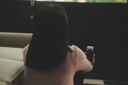 Depressed woman sitting alone on the bed with hands on head feel stress, sad and worried in the dark bedroom and low light environmentの写真素材