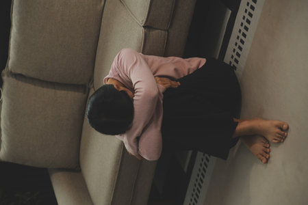 Depressed woman sitting alone on the bed with hands on head feel stress, sad and worried in the dark bedroom and low light environmentの写真素材