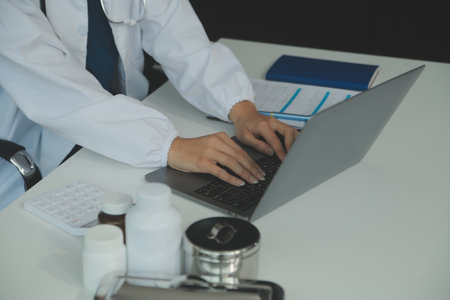 A beautiful and professional Asian female doctor is working on her medical cases on her laptop or making a video call medical consultation with a patient while sitting in her office.の写真素材